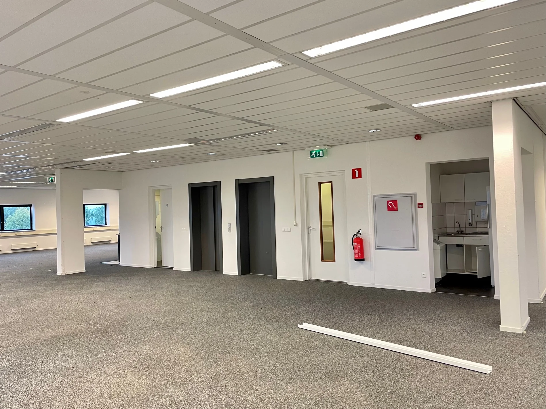 Kantoorruimte aan de Karel Doormanweg met tapijtvloer, liften, keukenblok en brandblusser.